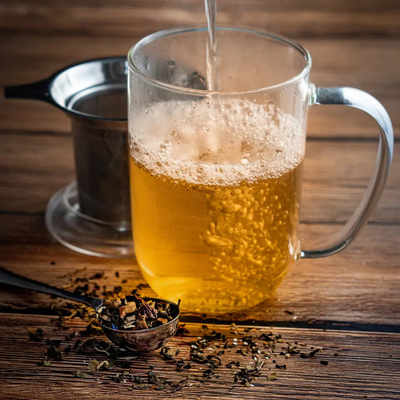 Steaming mug of loose leaf tea with tea leaves and blends arranged nearby